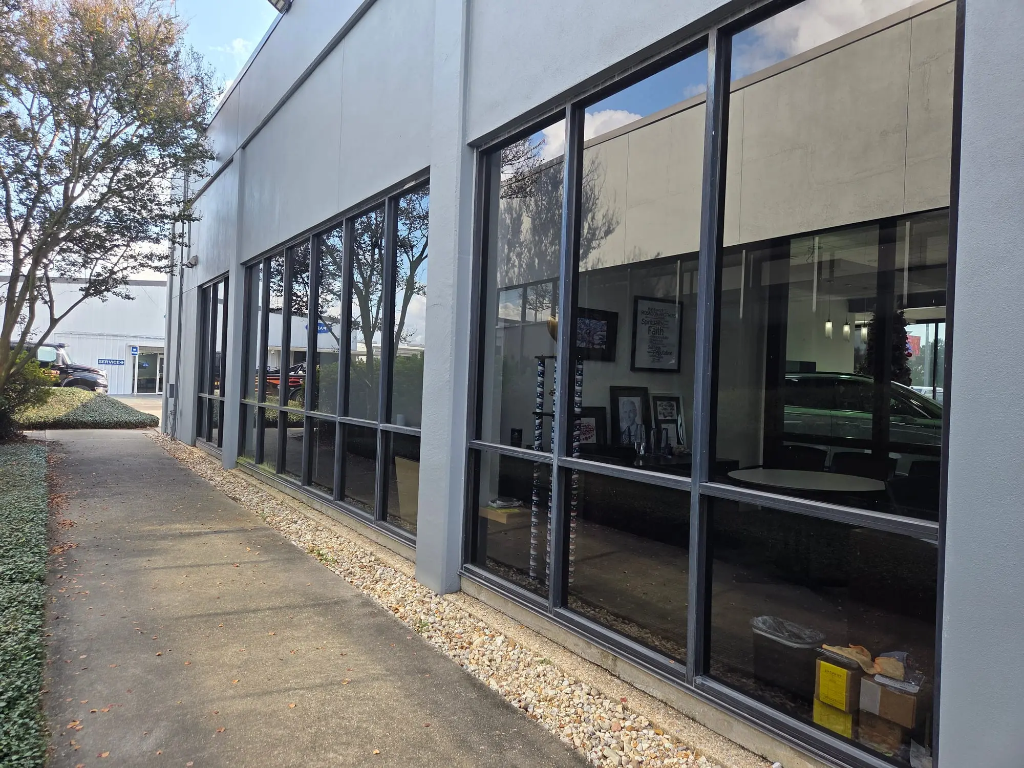A row of large, clean commercial windows along a sidewalk, reflecting trees and sky