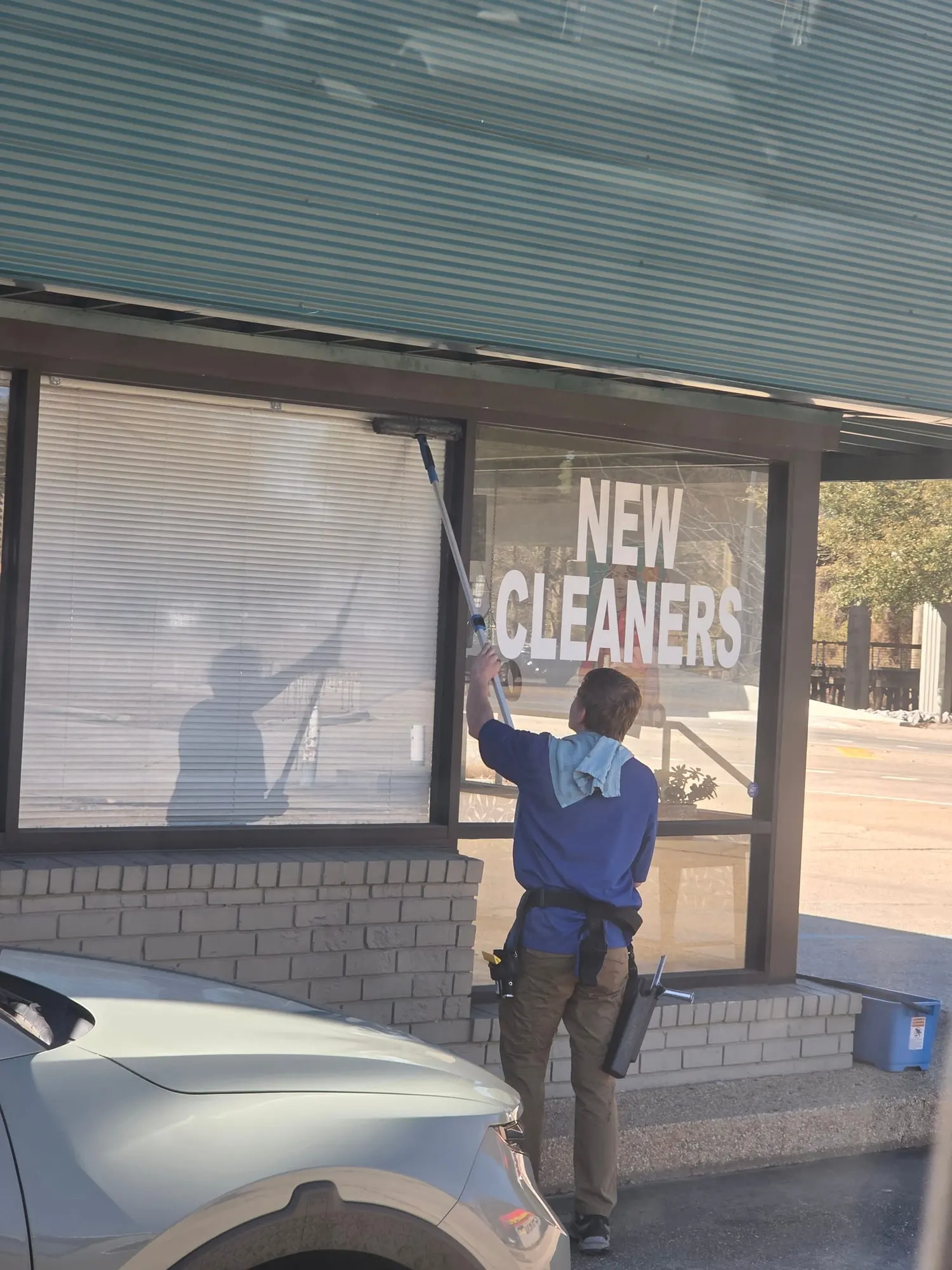 A window cleaner uses an extension pole to wash a storefront window under a metal awning