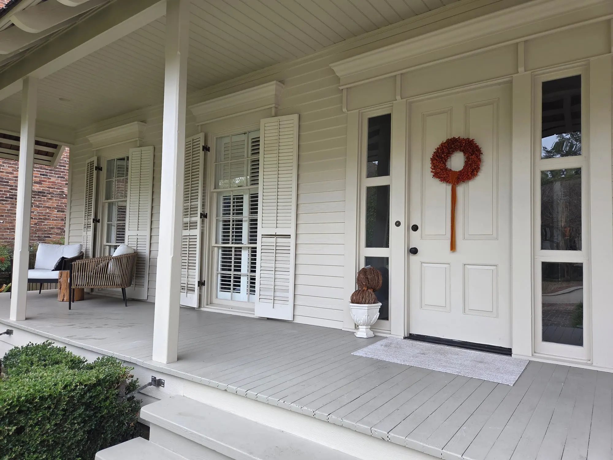 A front porch with clean double-hung windows, open shutters, and glass sidelights beside the door